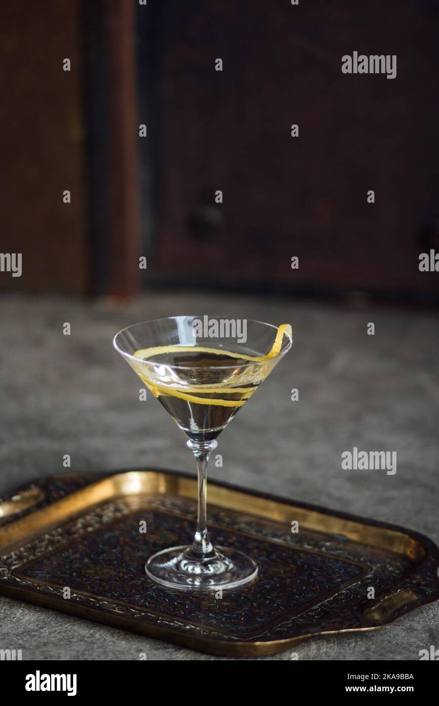 martini mit Zitronenverzierung auf verzierten indischen Messingtablett und Betonboden Stockfoto