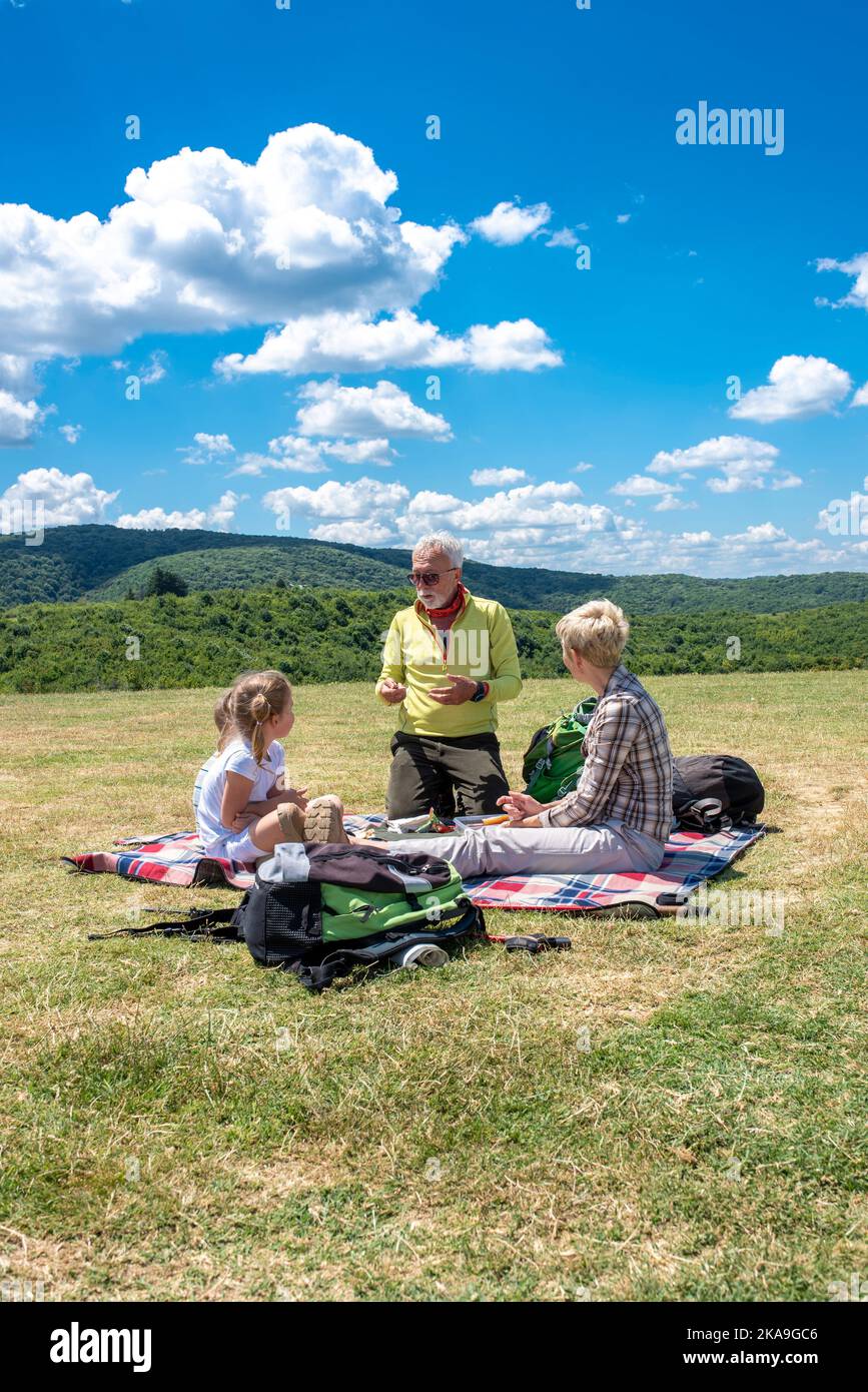 Eine vertikale Aufnahme einer Familie kaukasischer Menschen, die an einem sonnigen Tag auf einem offenen Feld ein Picknick machen Stockfoto
