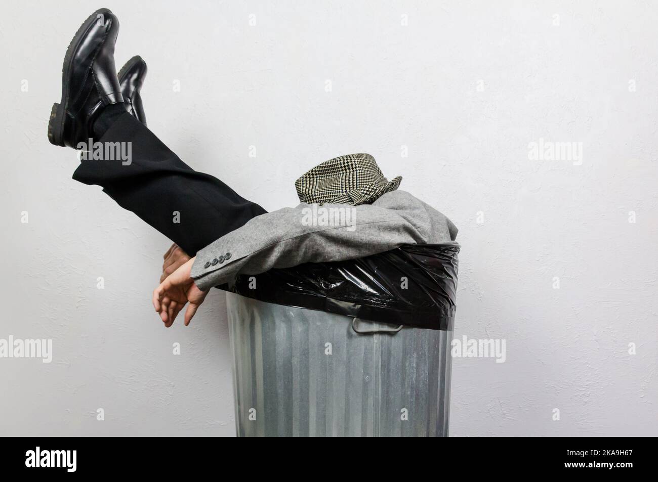 Porträt eines Geschäftsmannes in Anzug und Fedora-Hut im Trash Can. Der Mensch wird vom Kapitalismus und von Gier weggeworfen. Stockfoto