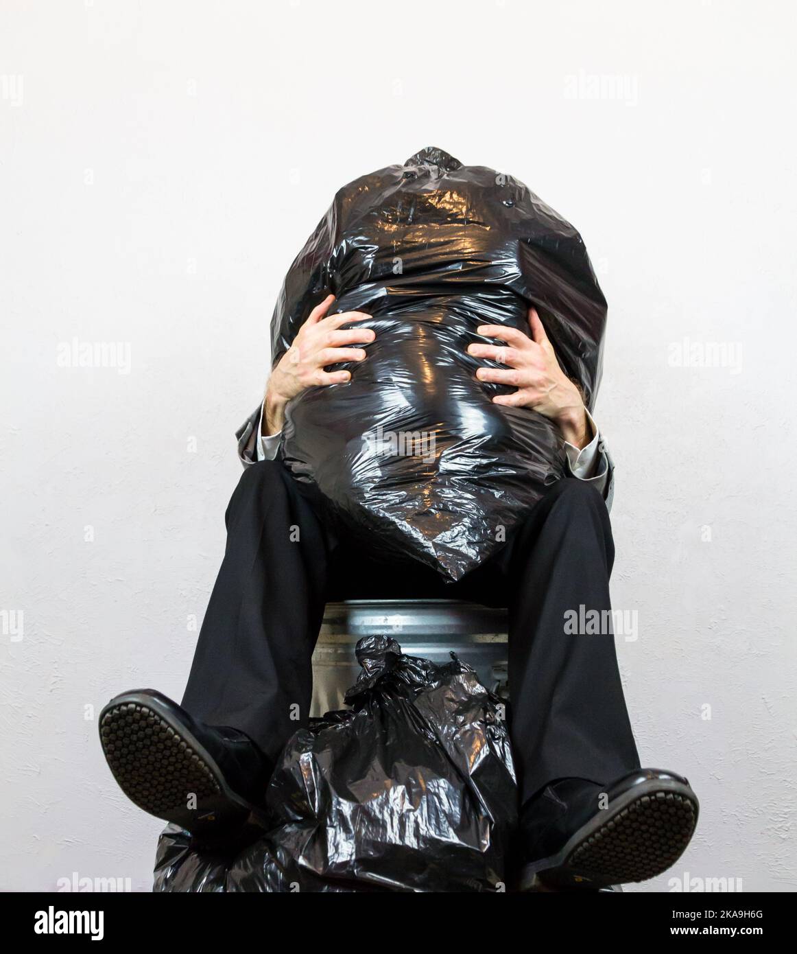 Portrait of man sitting in Trash Can crushed by Müll. Konzept des menschlichen Abfalls und Müllpersonals. Stockfoto