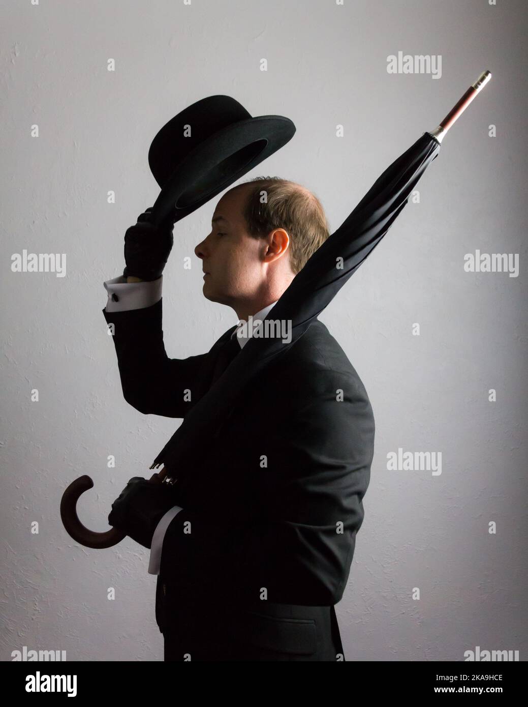 Profil Porträt eines britischen Geschäftsmannes in dunklem Anzug, der Bowler-Hut in höflicher Begrüßung und Regenschirm hält. Vintage Style des englischen Gentleman. Stockfoto