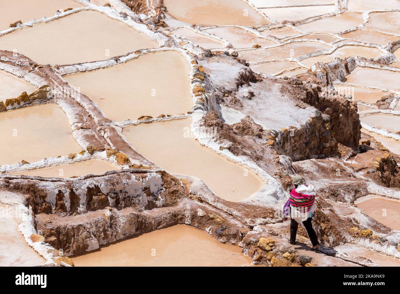 Mann, der in Maras Peru Salz extrahiert. Mann in farbenfrohen Kleidern, der Salz auf den Salzterrassen, genannt Maras, in der Nähe von Cusco, Peru, absaugt Stockfoto