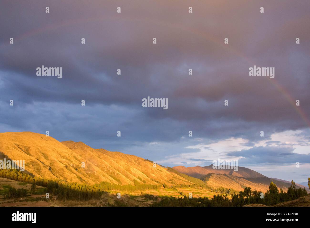 Sonnenstrahlen treffen die Berge unter einem stürmischen blauen und grauen Himmel im Heiligen Tal, in der Nähe von Cusco, Peru. Der genaue Ortsname lautet Pucapucara. Stockfoto