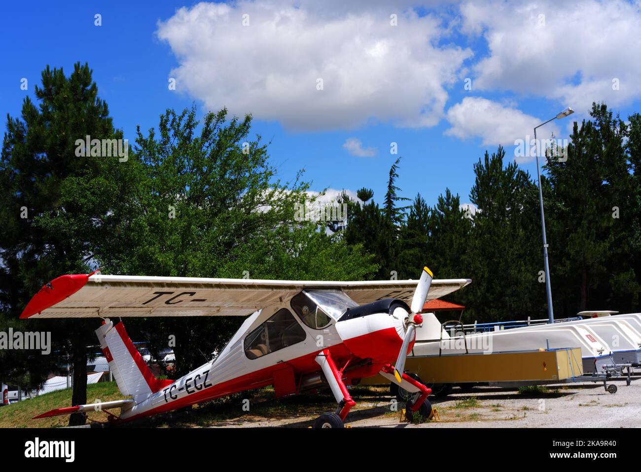 Weißes Flugzeug, das an einem sonnigen Tag unter bewölktem Himmel in Bäumen geparkt ist Stockfoto