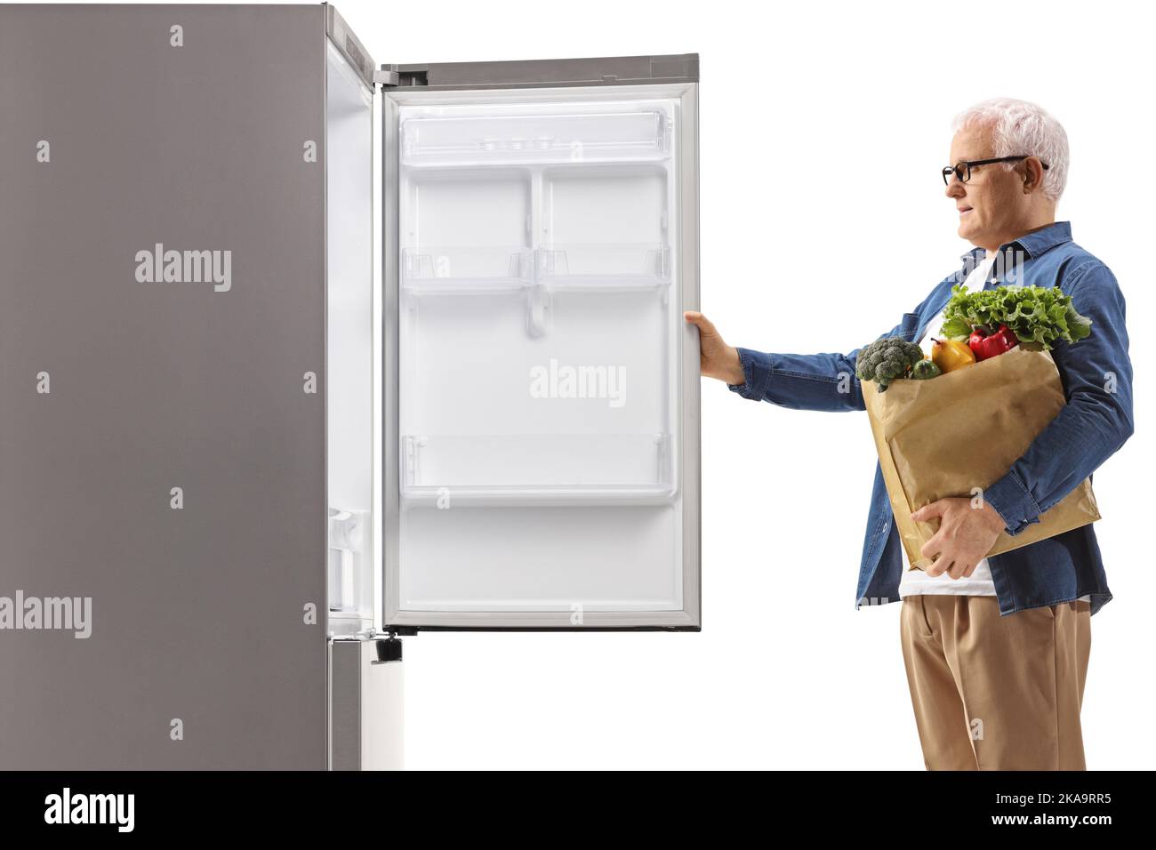 Profilaufnahme eines reifen Mannes mit einer Einkaufstasche, die einen Kühlschrank öffnet, isoliert auf weißem Hintergrund Stockfoto
