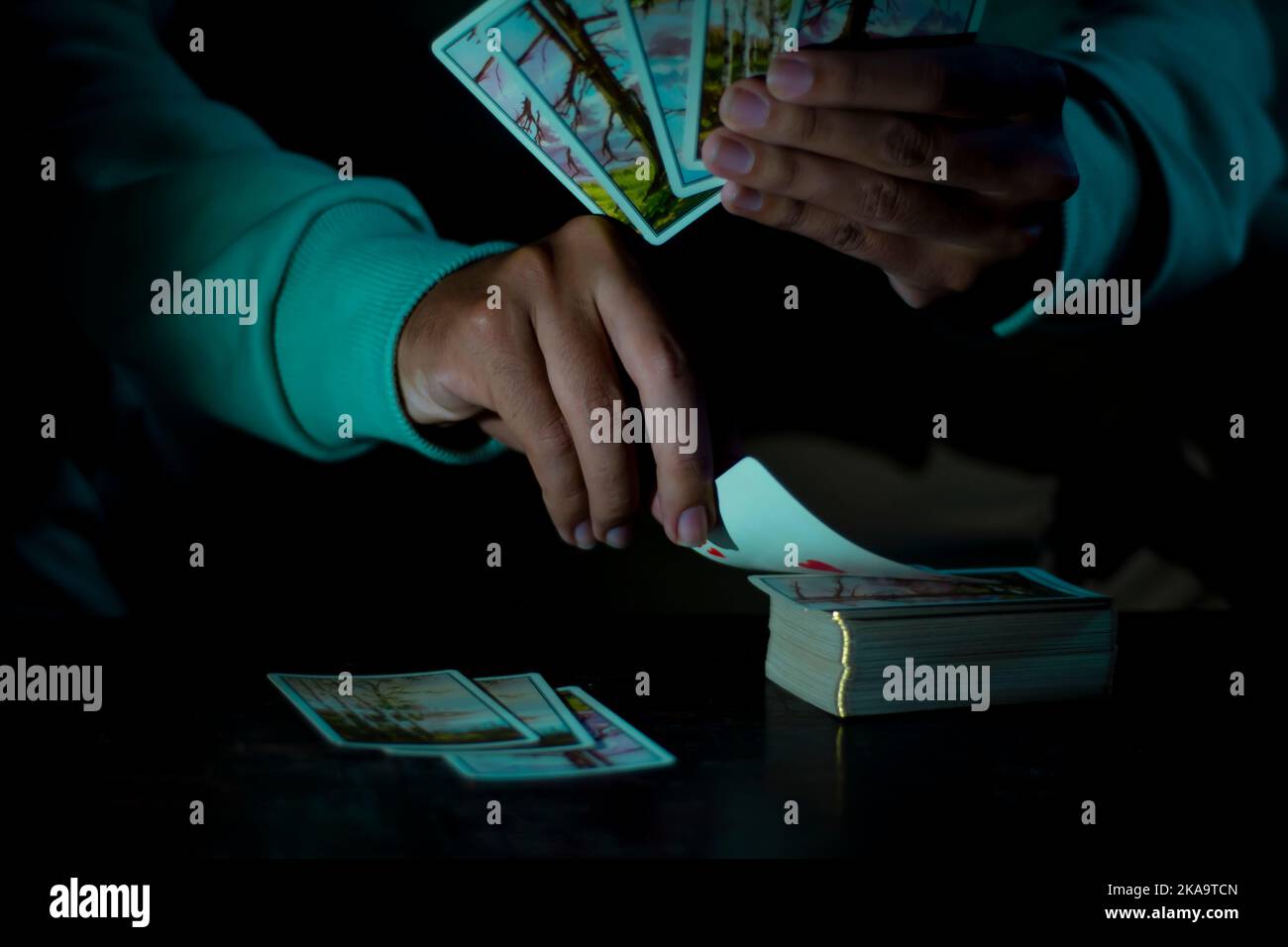 Ein Mann, der mit Karten auf einem Tisch in einem dunklen Hintergrund spielt Stockfoto