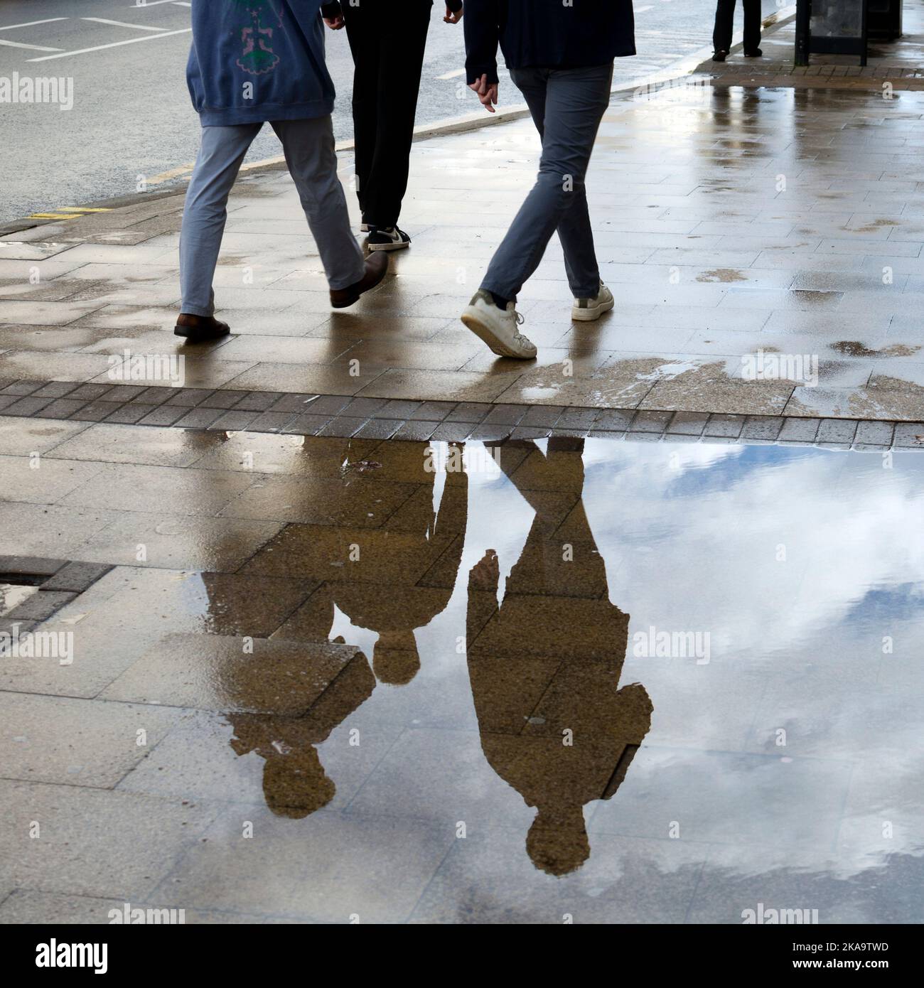 Drei Personen gehen, reflektiert in einer Pfütze, Leamington Spa, Großbritannien Stockfoto
