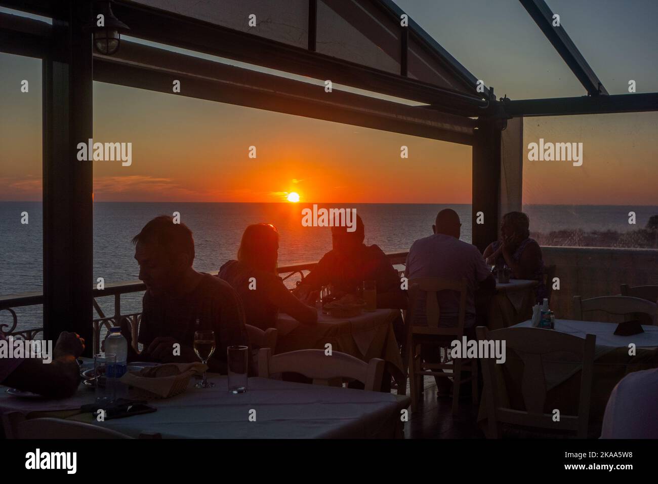 Goldener Sonnenuntergang über der Ägäis im Ferienort Molyvos auf der griechischen Insel Lesvos Griechenland mit Menschen, die in einem Tavernenrestaurant essen Stockfoto
