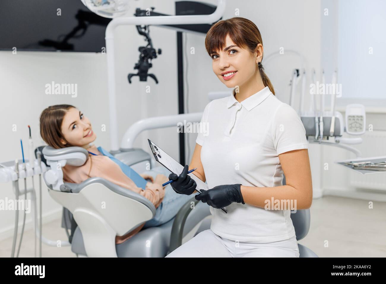 Freundlicher Zahnarzt mit Tablette auf dem Hintergrund des Patienten während der Zahnuntersuchung. Moderne Zahnklinik. Konzept der professionellen Mundpflege, Beratung Stockfoto