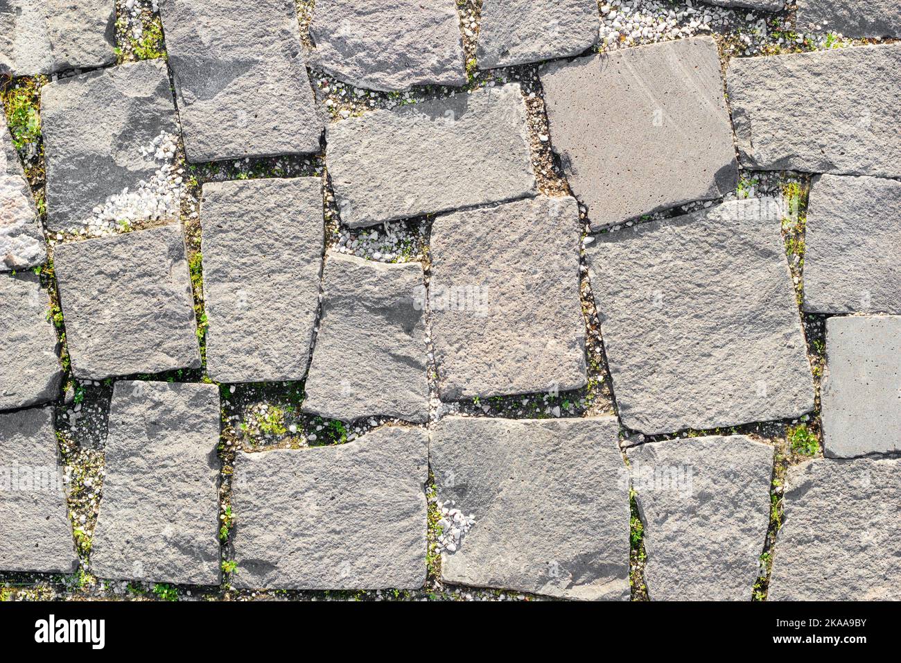 Struktur von gemauerten Straßen aus asymmetrischen Steinen mit Gras zwischen Mauerwerk. Draufsicht Stockfoto