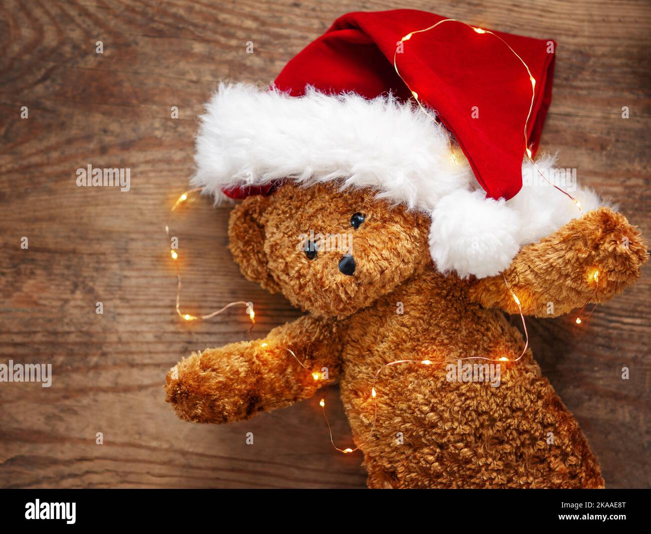 Teddybär im Weihnachtsmannhut. Plüschtier mit Glühbirnen auf schäbigen Holzhintergrund. Neujahr. Stockfoto