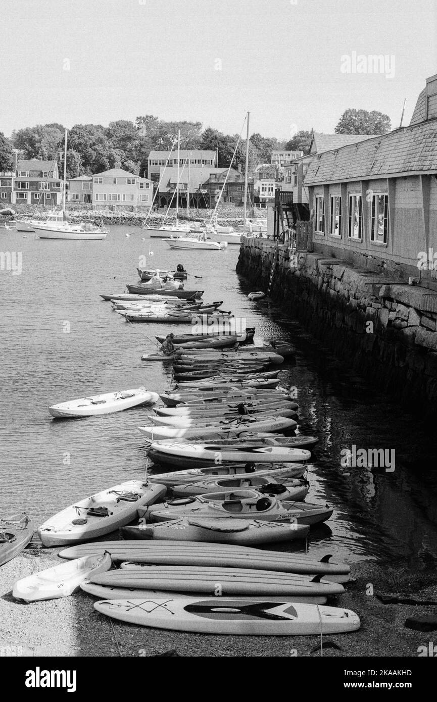 Eine lange Reihe von Kajaks ankerte im Wasser entlang eines Piers in Rockport, Massachusetts. Das Bild wurde auf analogem Schwarzweiß-Film aufgenommen. Stockfoto