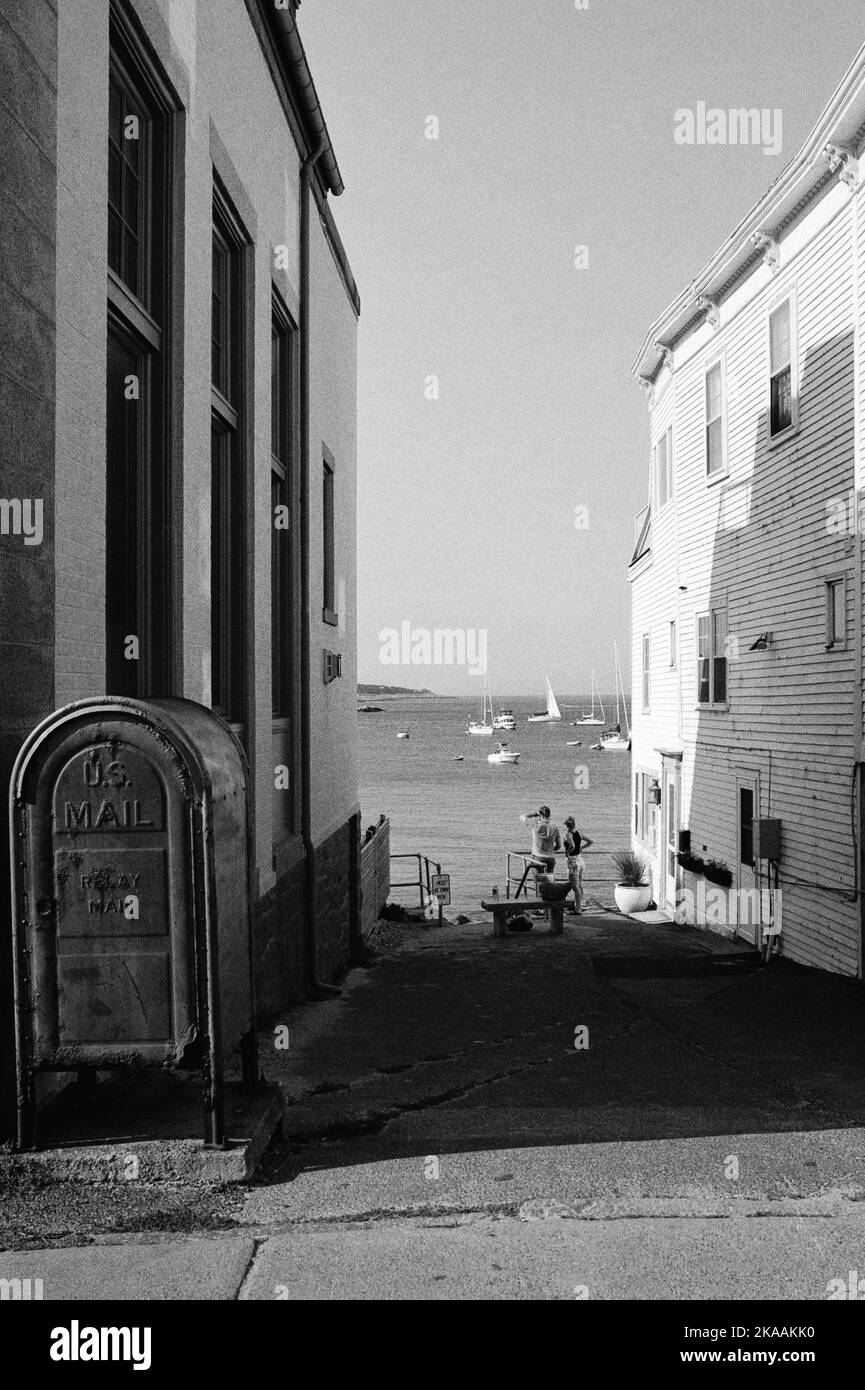 Ein junges Paar steht an der Treppe, die zwischen zwei Gebäuden in Rockport, Massachusetts, zum Ufer führt. Das Bild wurde mit analoger Schwarzweißaufnahme aufgenommen Stockfoto