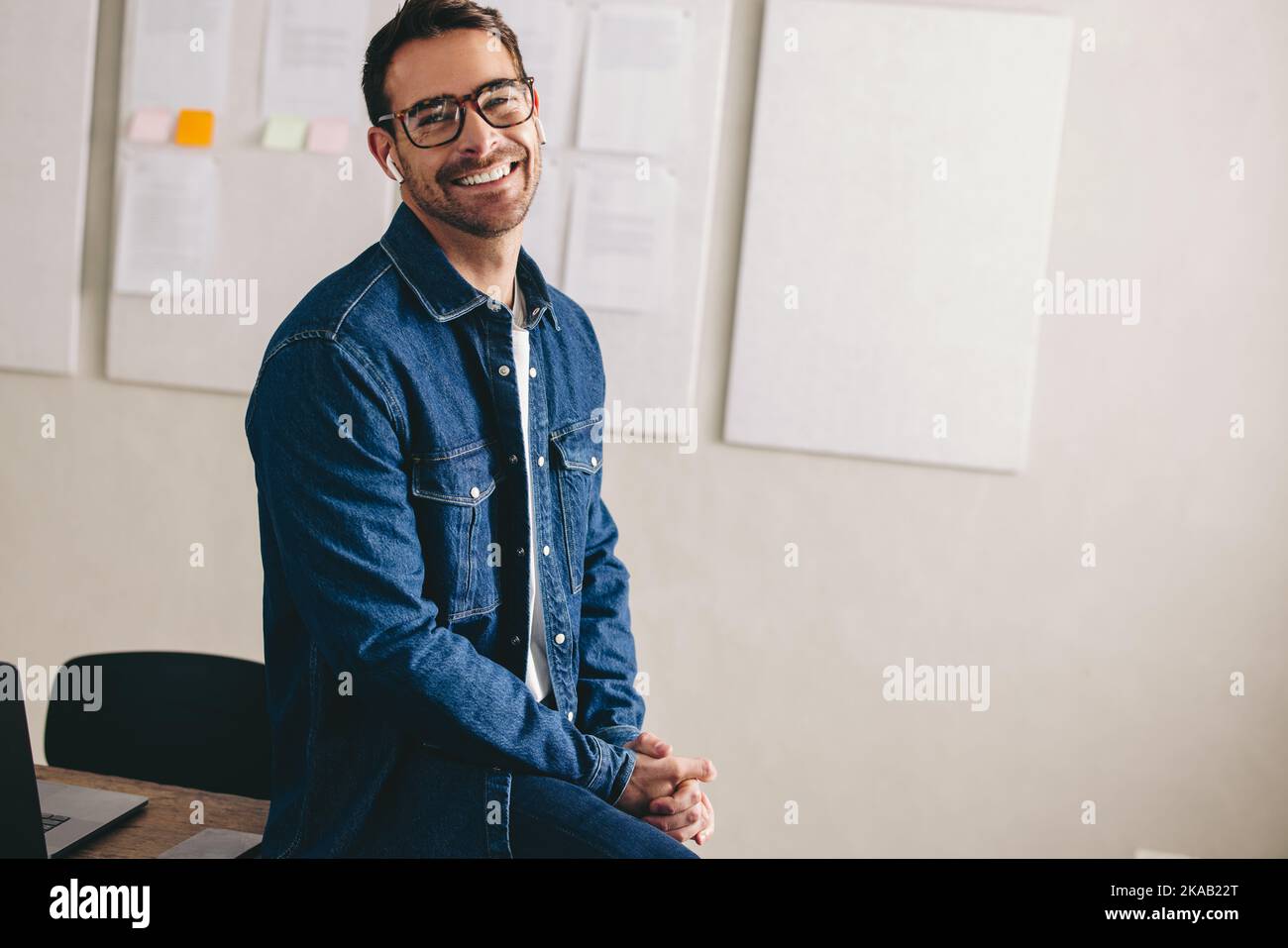 Glücklicher junger Geschäftsmann, der mit schnurlosen Ohrhörern eine Konferenzschaltung führt. Fröhlicher Geschäftsmann lächelt, während er mit seinem Team kommuniziert. Geschäftsmann mit Stockfoto