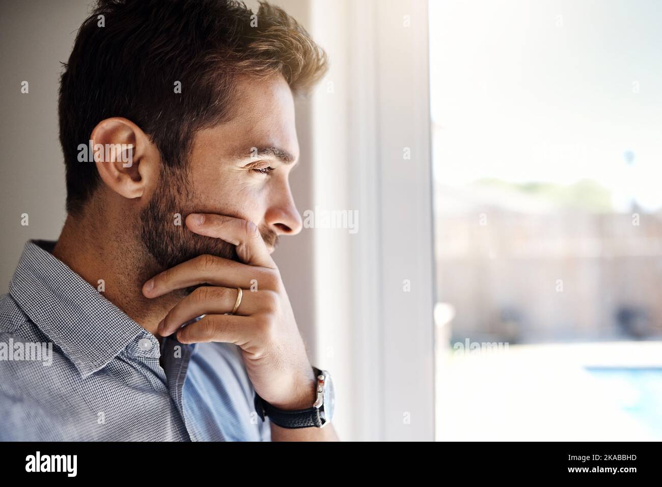 HES denkt darüber nach, etwas an seinem Leben zu ändern. Ein fokussierter junger Mann, der tagsüber durch ein Fenster schaut, während er zu Hause nachdenkt. Stockfoto