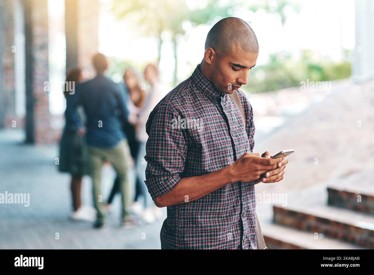 Teilt seinen ersten College-Tag mit Social Media. Ein junger Mann, der ein Mobiltelefon im Freien auf dem Campus benutzt. Stockfoto