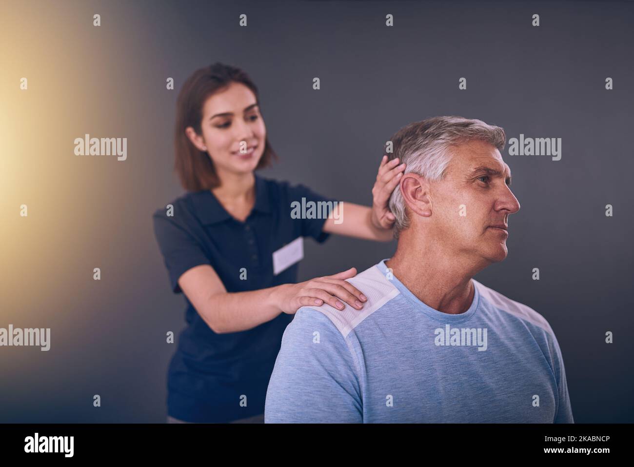 Schauen Sie mir zur Seite. Eine junge Physiotherapeutin, die einen reifen männlichen Patienten behandelt. Stockfoto