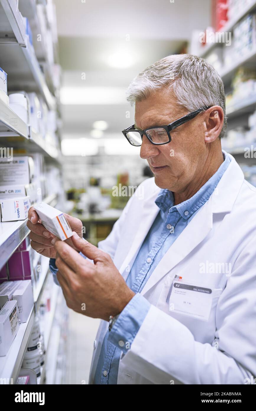 Dies hält Sie von Übelkeit ab. Ein fokussierter reifer Apotheker hält eine Medikamentenkiste in der Hand und liest sie in einer Apotheke. Stockfoto