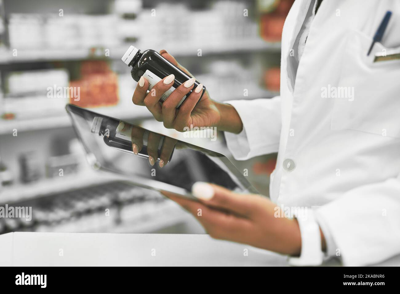 Wir brauchen mehr von dieser Art. Eine unverkennbare Apothekerin, die eine digitale Tablette in der einen Hand und Medikamente in der anderen innerhalb einer Apotheke hält. Stockfoto