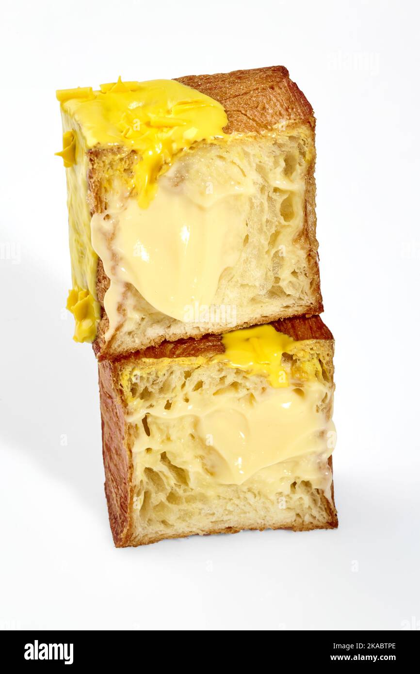 In Scheiben geschnittenes, flauschiges, würfelförmiges Croissant mit Vanillepudding, gelber Glasur und Schokoladenstückchen Stockfoto