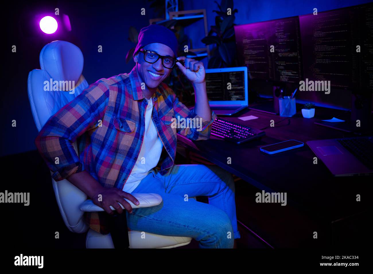 Profilportrait von positiven Hacker Kerl sitzen Stuhl berühren Brillen verbessern Cybersecurity-Server am späten Abend in Innenräumen Stockfoto