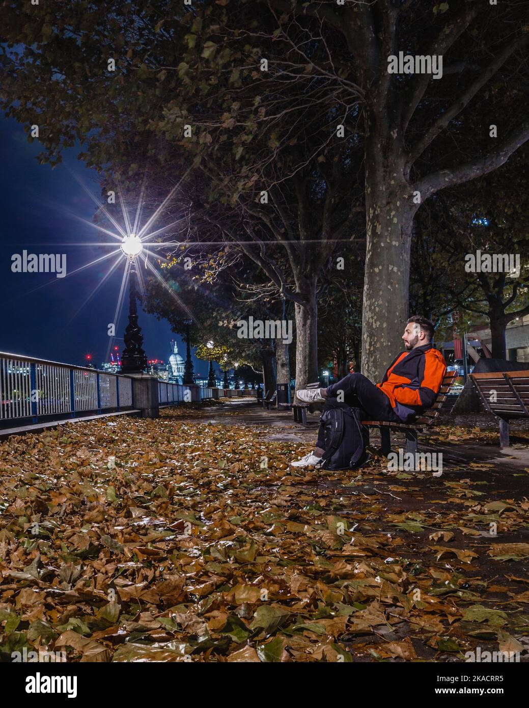 Ein eintönige Londoner sitzt auf einer Bank inmitten der Herbstblätter am Londoner South Bank. Stockfoto Ein eintönige Londoner sitzt auf einer Bank inmitten der Herbstblätter am Londoner South Bank. Stockfoto