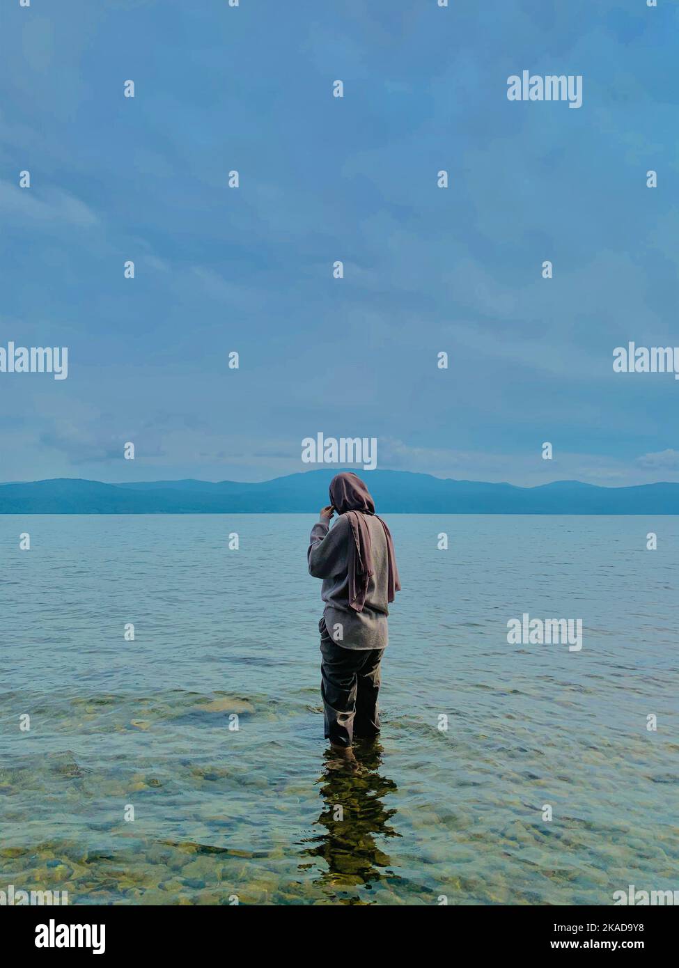 Ein Mädchen mit Hijab, das im Meer steht und den Moment unter bewölktem Himmel genießt Stockfoto