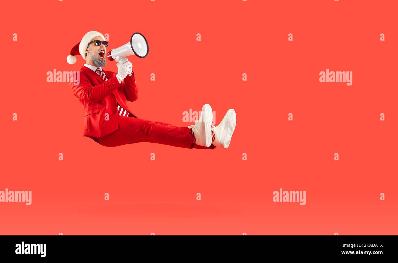 Glücklicher Mann, der auf rotem Hintergrund schwebt, für Weihnachtsverkäufe wirbt und durch das Megaphon schreit Stockfoto