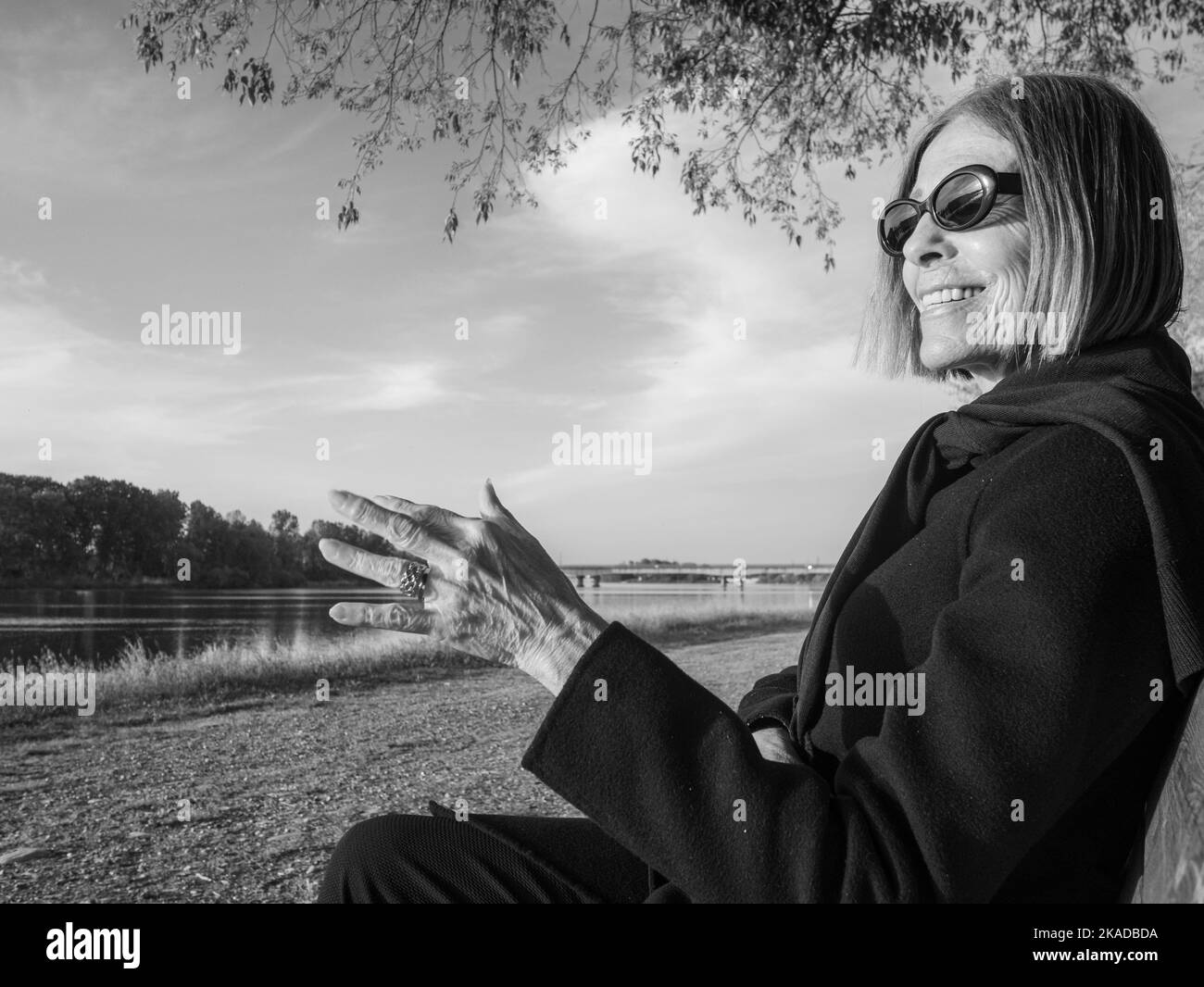 Erwachsene, reife, elegante kaukasische Frau, die im Frühling auf einer Parkbank mit gekreuzten Beinen sitzt Stockfoto