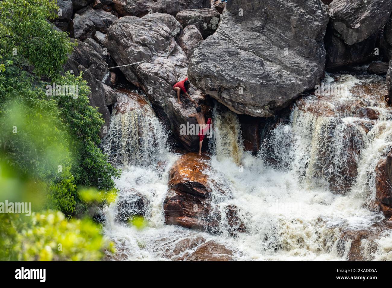 Ein junger Mann, der versucht, einen Felsen im Wasserfall am Fuße des Berges Tepui zu erklimmen. Tepequém, Bundesstaat Roraima, Brasilien. Stockfoto