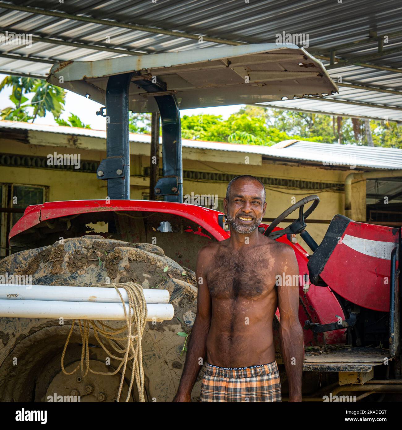 Ein schwarzer Mann, der vor seinem roten Traktor steht und lächelt Stockfoto