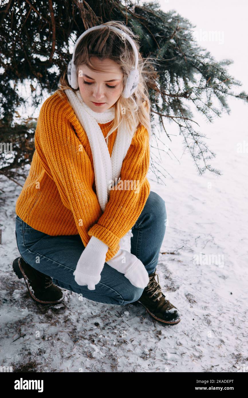 Teen blond in einem gelben Pullover draußen im Winter. Ein Teenager-Mädchen auf einem Spaziergang in Winterkleidung in einem verschneiten Wald. Stockfoto