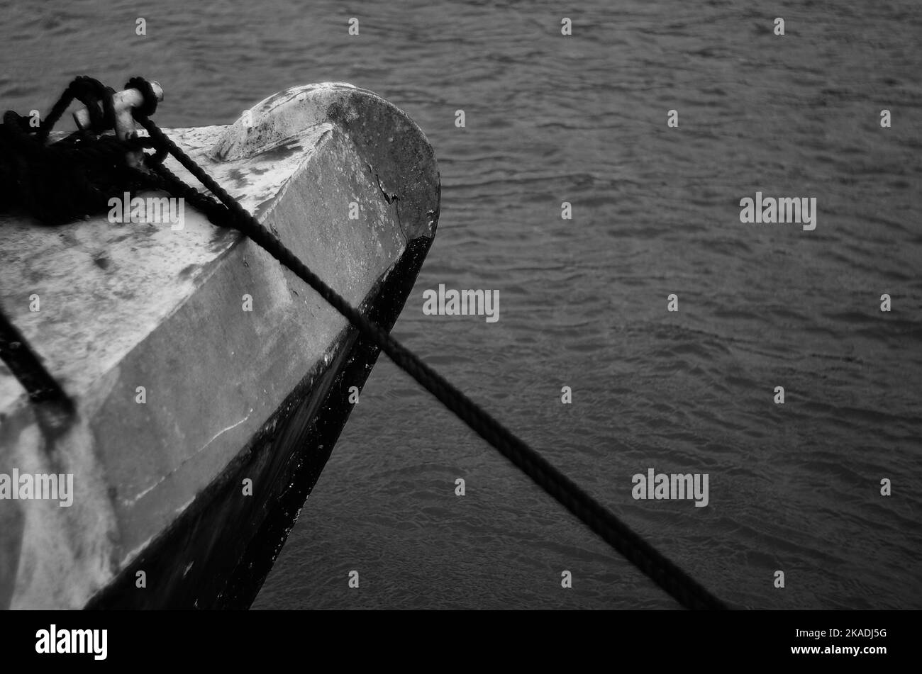 Eine Nahaufnahme eines rostigen metallischen Randes eines Bootes, das mit Seilen im Wasser eingewickelt ist und in Graustufen geschossen wurde Stockfoto