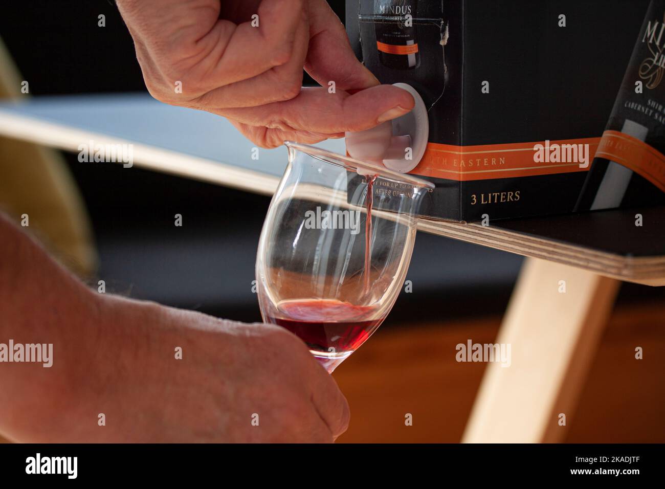 Von Hand Rotwein aus einem BIB - Pappbeutel in einem Karton mit offenem Hahn auf einem Tisch stehend in ein Glas gießen. Nahaufnahme des Bildes. Kopenhagen, Dänemark - November Stockfoto