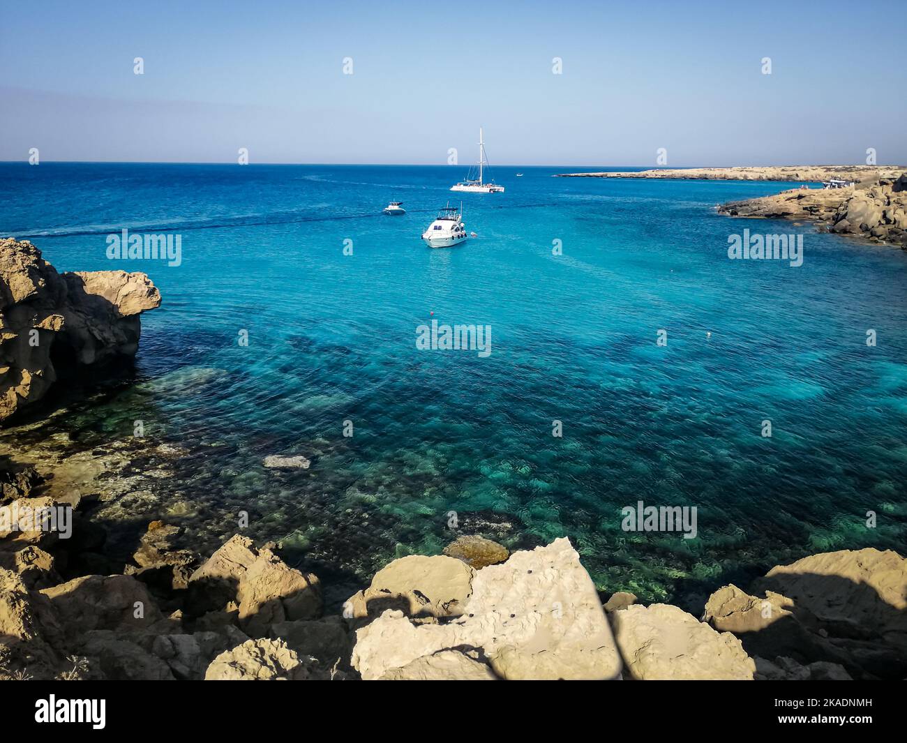 Blick auf das Meer und die Klippen der Blauen Lagune, Cape Greco, Zypern. Kleine Boote vor Anker in der Bucht. Stockfoto