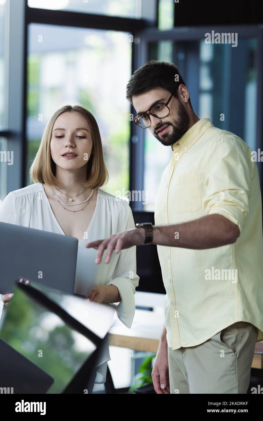 Geschäftsmann zeigt auf Laptop in der Nähe eines neuen Mitarbeiters im Büro, Bild aus dem Stock Stockfoto