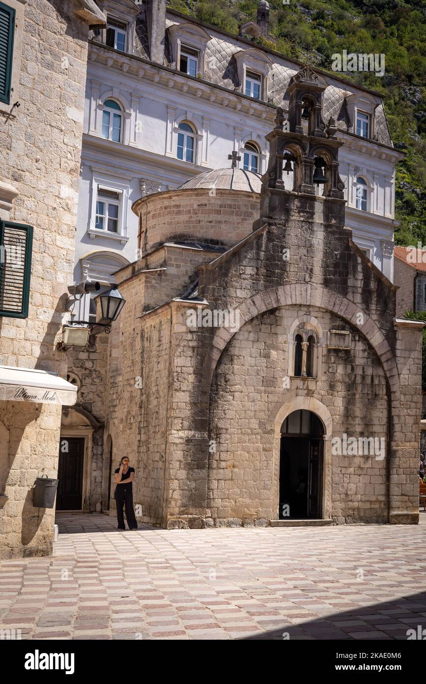 Kotor, Montenegro - 29. April 2022: Die Fassade einer mittelalterlichen orthodoxen St. Lukes Kirche in der Altstadt von Kotor. Eine schwarz gekleidete Frau steht an der Mauer. Stockfoto