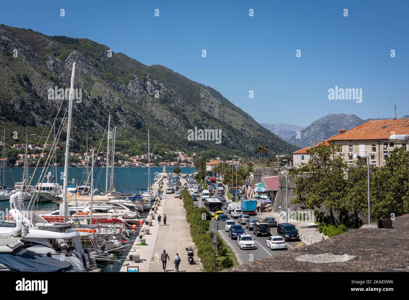 Kotor, Montenegro - 29. April 2022: Menschen auf einer Promenade in der Altstadt von Kotor, Boote und Schiffe liegen am Pier vor. Berge im Hintergrund. Stockfoto