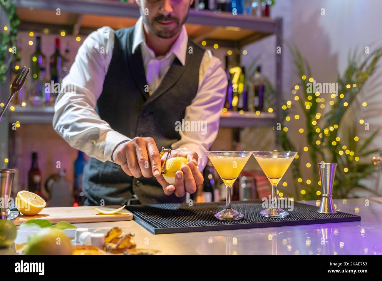 Ein hübscher junger Barkeeper, der im Nachtclub an der Bartheke elegante Cocktails mit Lichtern bei der Nachtklubparty zubereitet. Stockfoto
