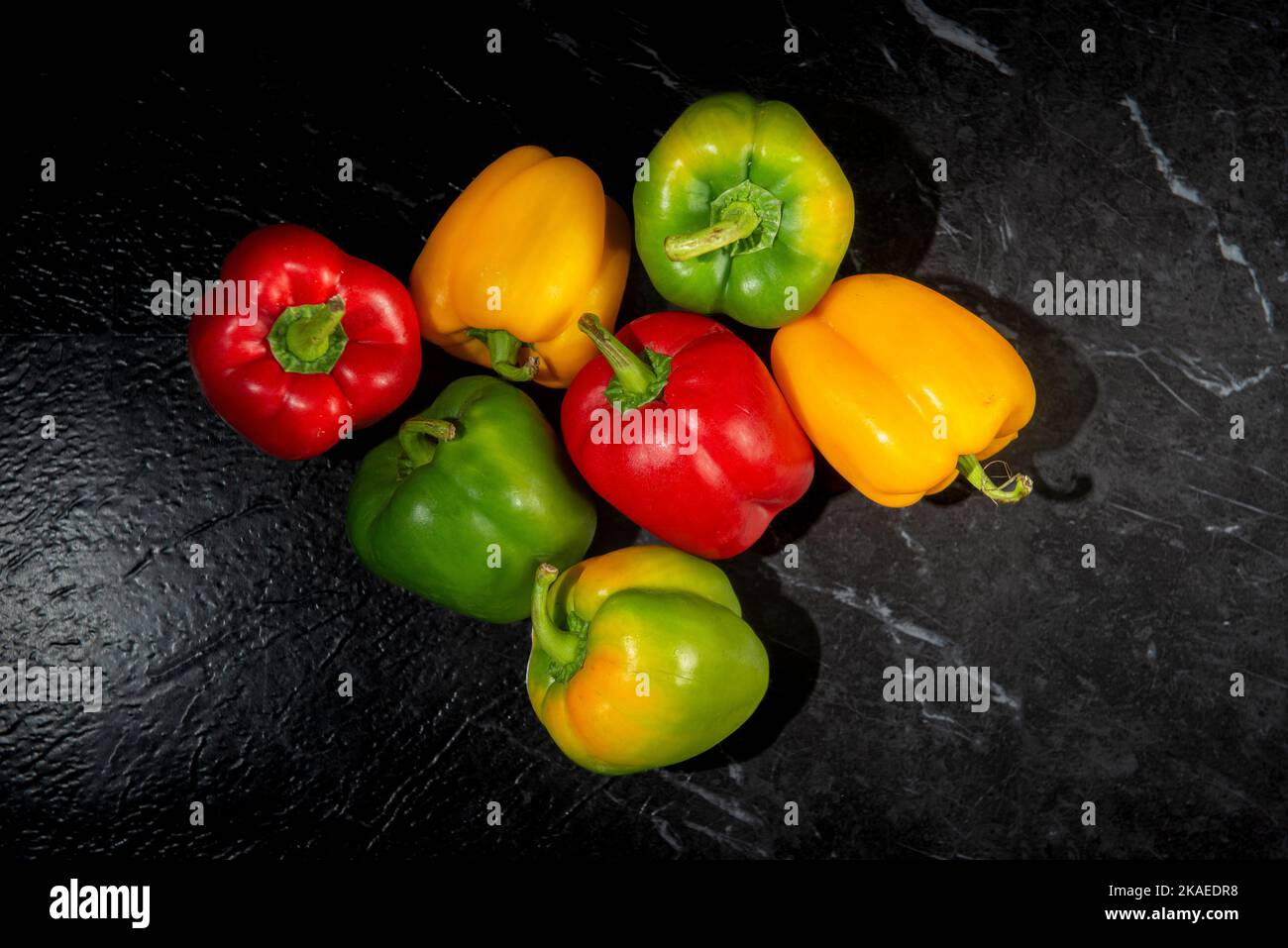 Grüne rote und gelbe Paprika auf einer Arbeitsfläche aus schwarzem Marmor. Stockfoto