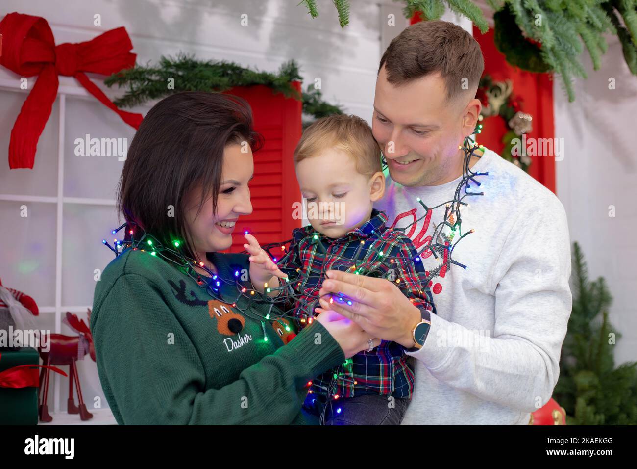 Die dreiköpfige Familie umarmt sich am weihnachts-Drehort mit roten und grünen Dekorationen. Fröhliche Mutter, Vater und kleiner Sohn hingen mit Stockfoto