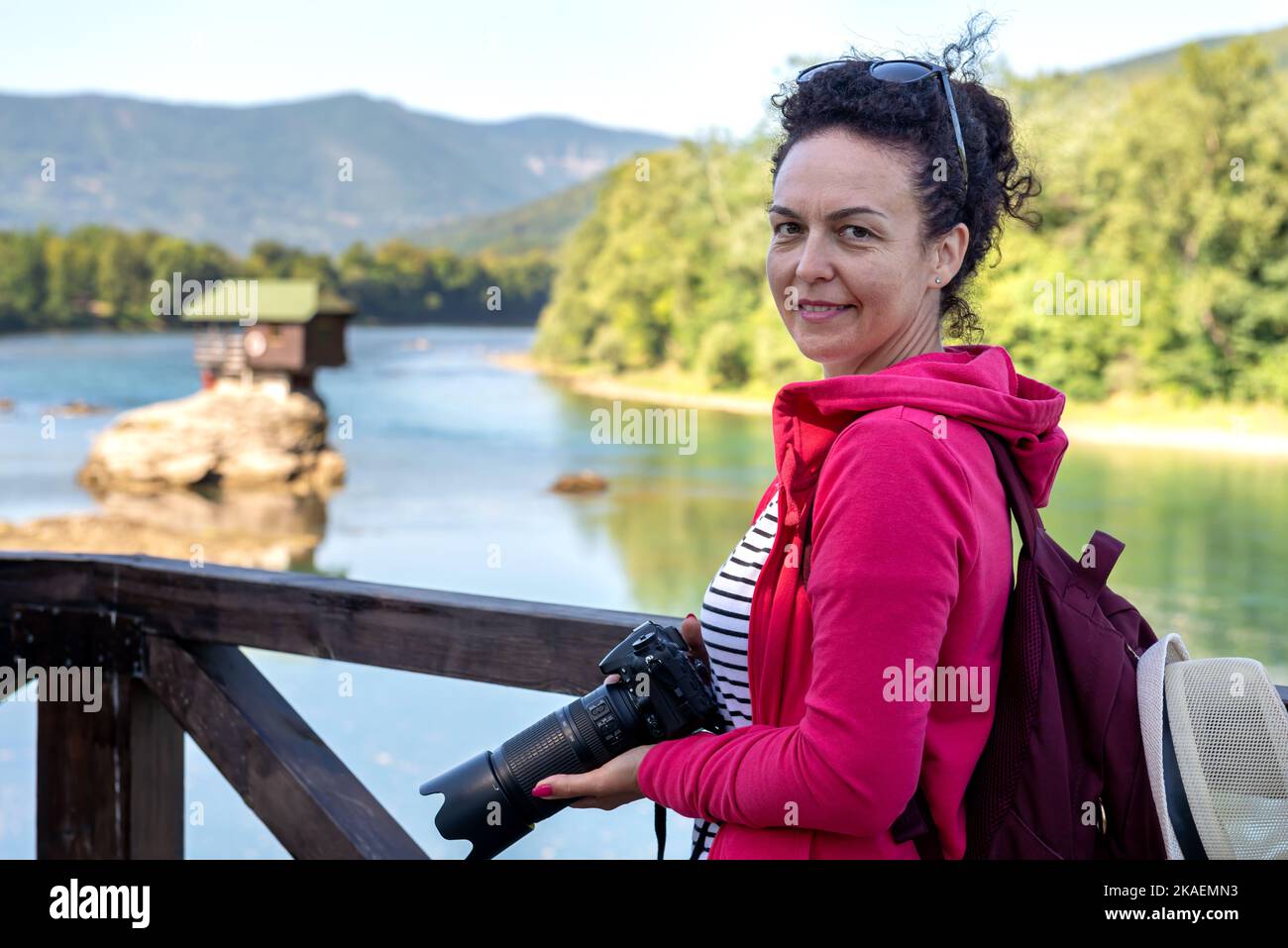 Eine Frau hält eine dslr-Kamera vor einem beliebten Touristenort am Fluss Drina in Serbien. Stockfoto