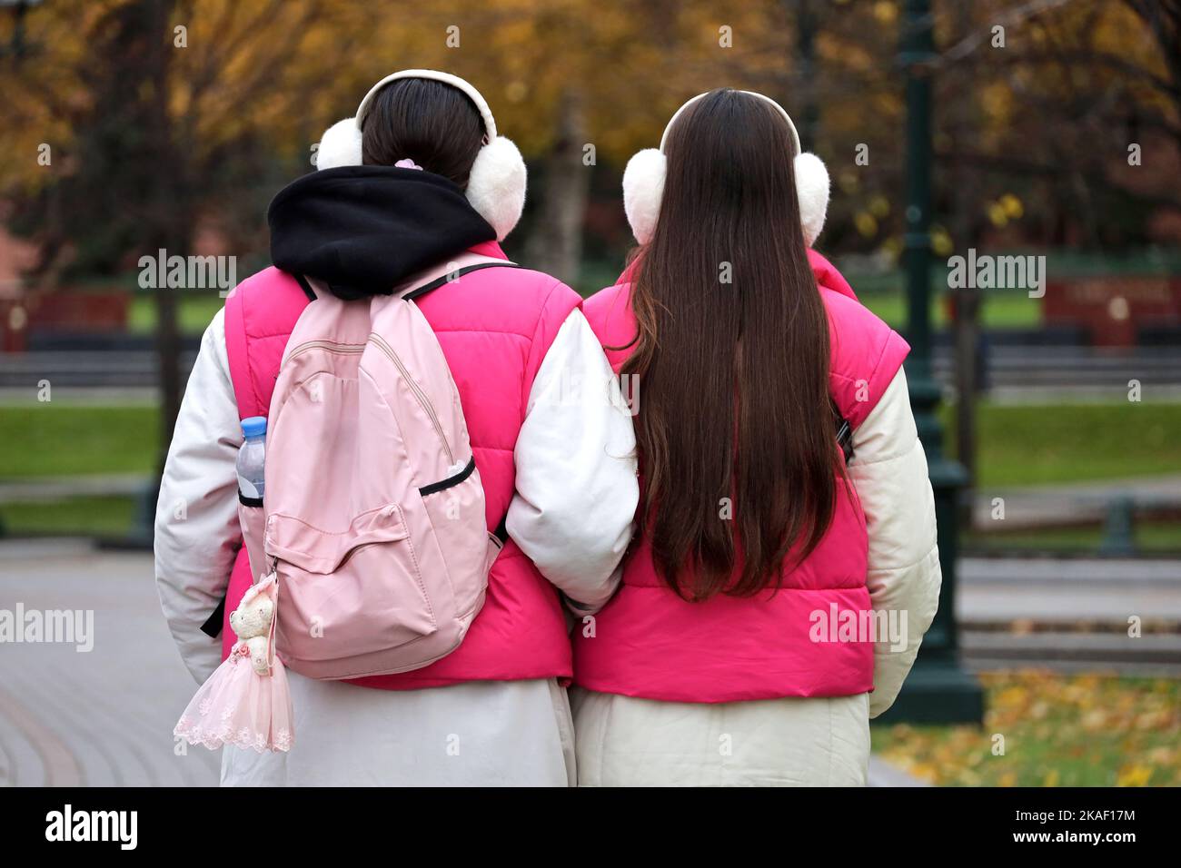 Zwei Mädchen in der gleichen Kleidung und Ohrenschützer, die auf einer Stadtstraße spazieren. Zwillinge im Herbstpark Stockfoto