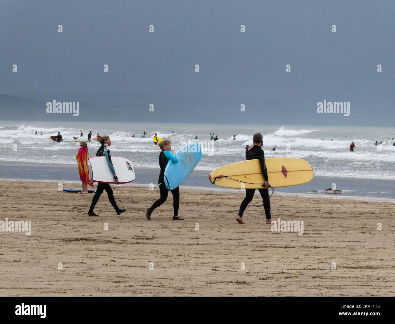 Drei Freunde tragen Surfbretter zum Wasser in Saunton Sands in Devon England Stockfoto