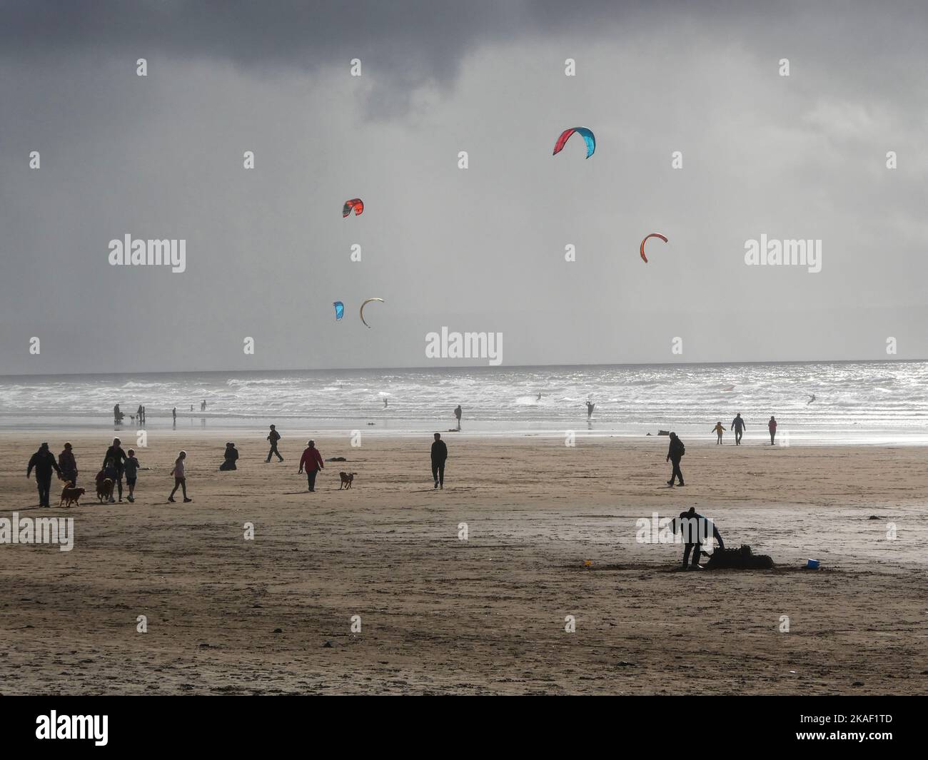 Menschen, die am Strand spazieren, während Windsurfer im Meer in Saunton Sands in Devon, Großbritannien, spielen Stockfoto