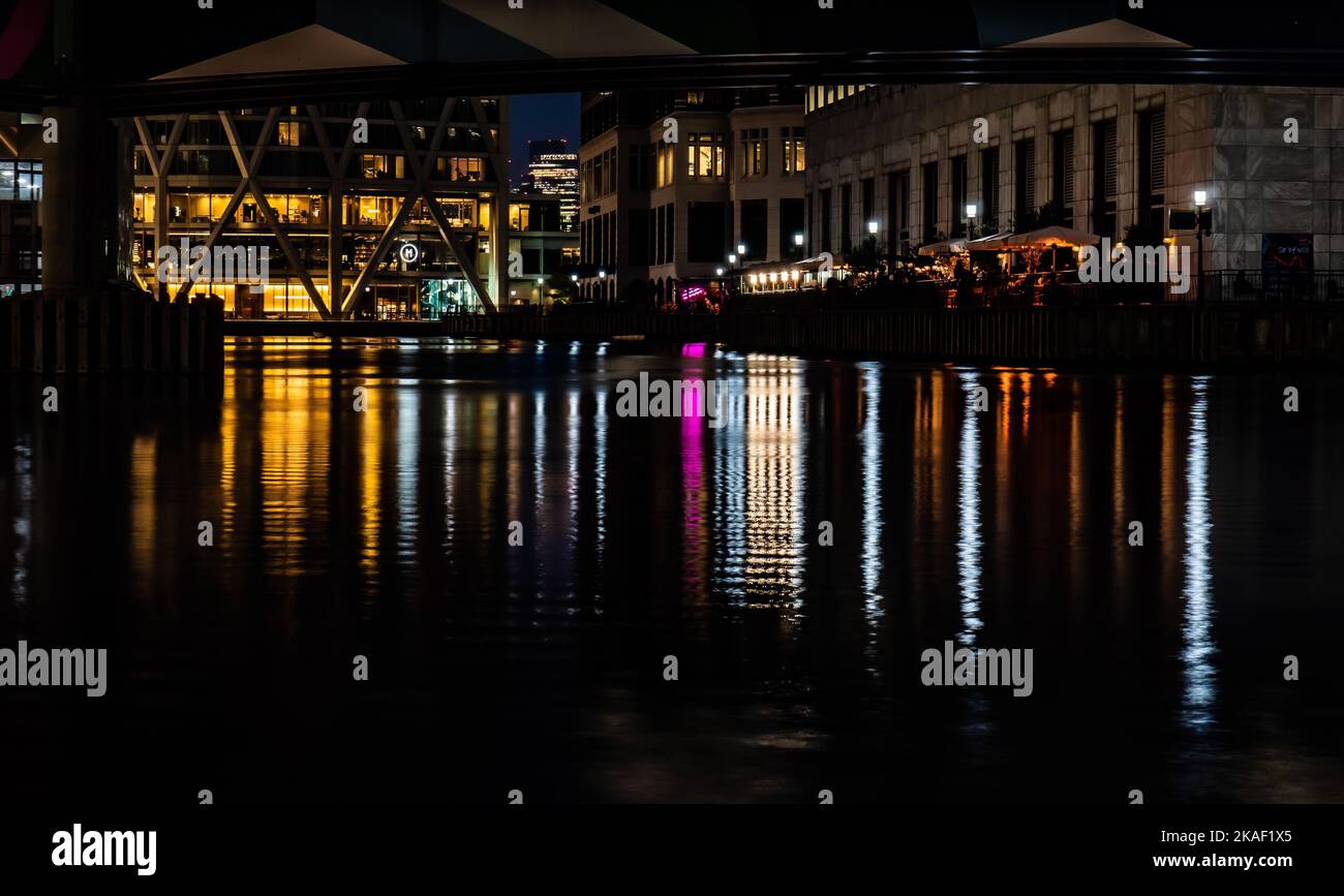 Bunte Stadtlichter, die sich auf dem Wasser spiegeln, mit Gebäuden im Hintergrund. Stockfoto