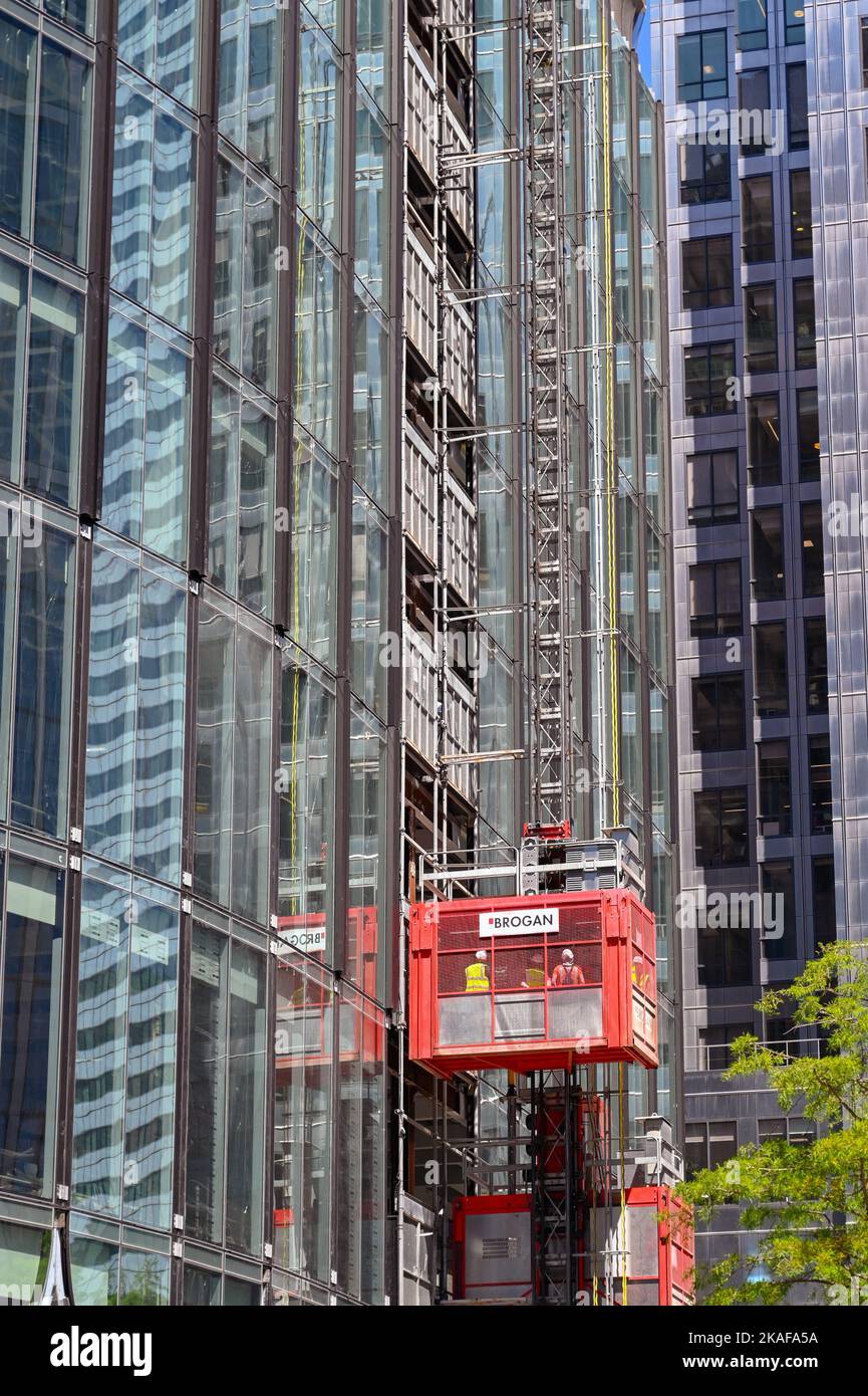 London, England - 2022. Juni: Bauarbeiter fahren mit einem Aufzug auf der Außenseite eines neuen Büroblocks, der im Bau ist Stockfoto