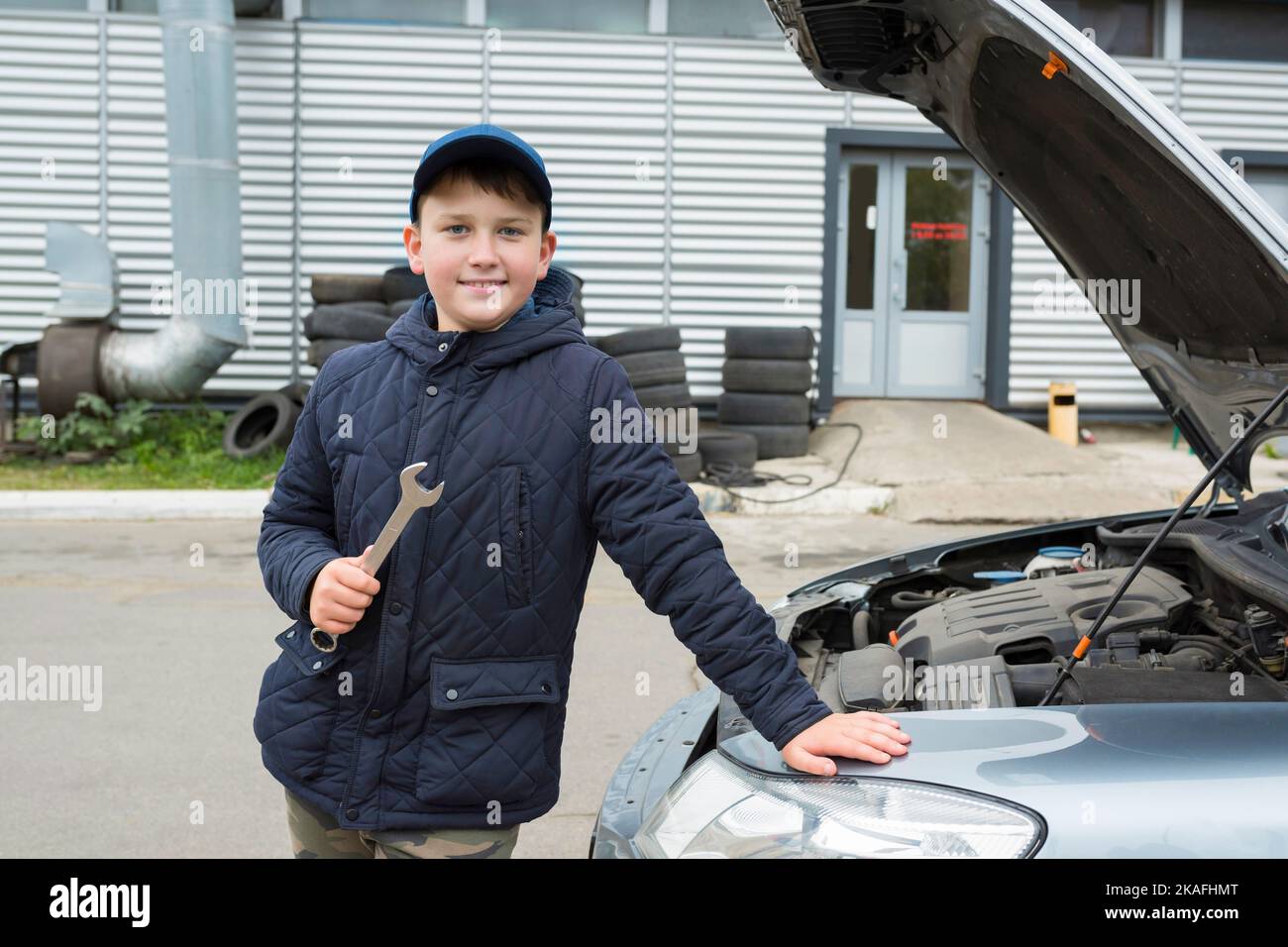 Glücklicher Teenager-Junge mit Schraubenschlüssel beim Autoservice, hilft Vater. Reparaturservice Stockfoto