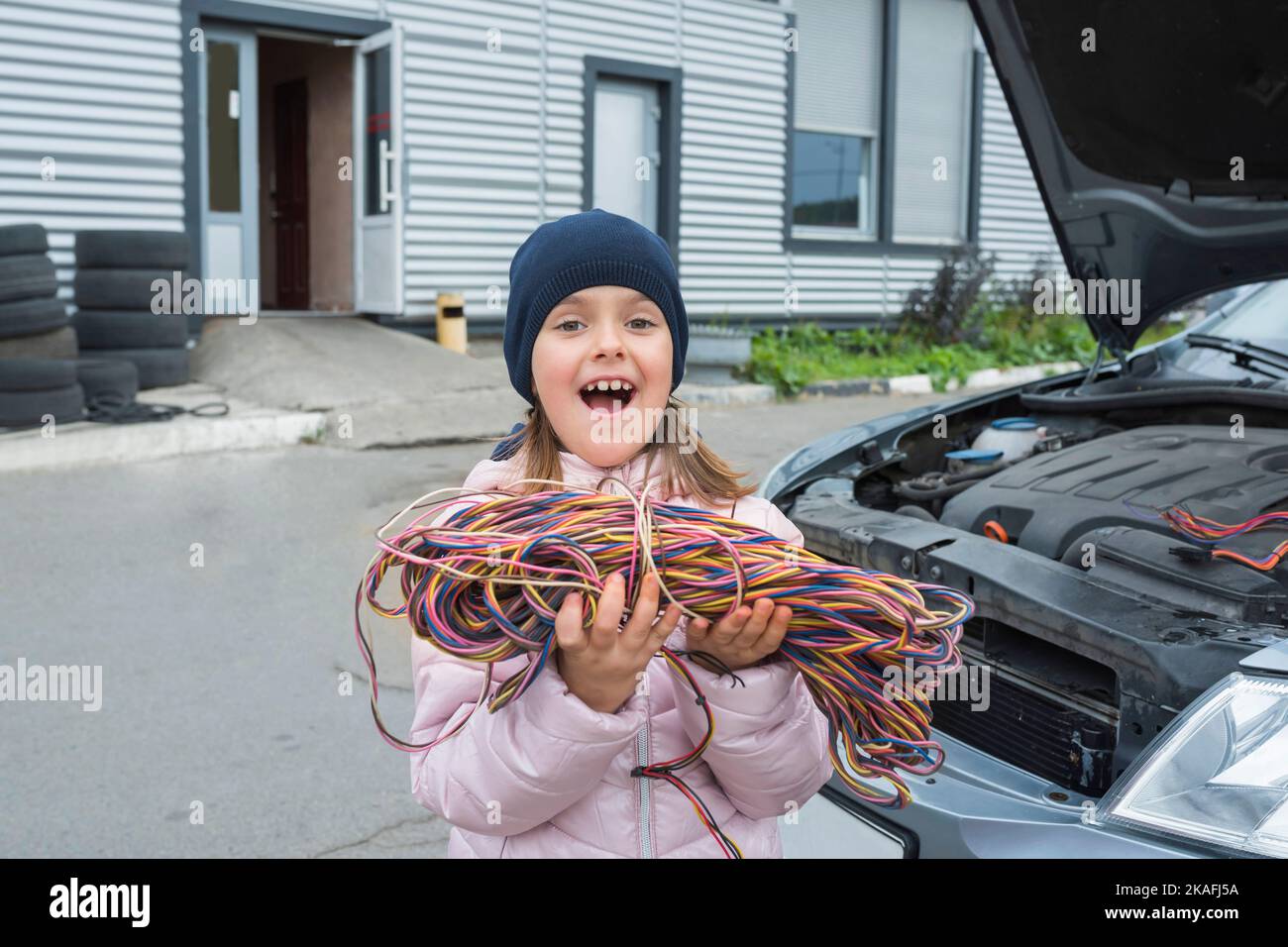 Ein kleines Mädchen mit einem Draht in den Händen arbeitet in der Garage. Autoservice Stockfoto