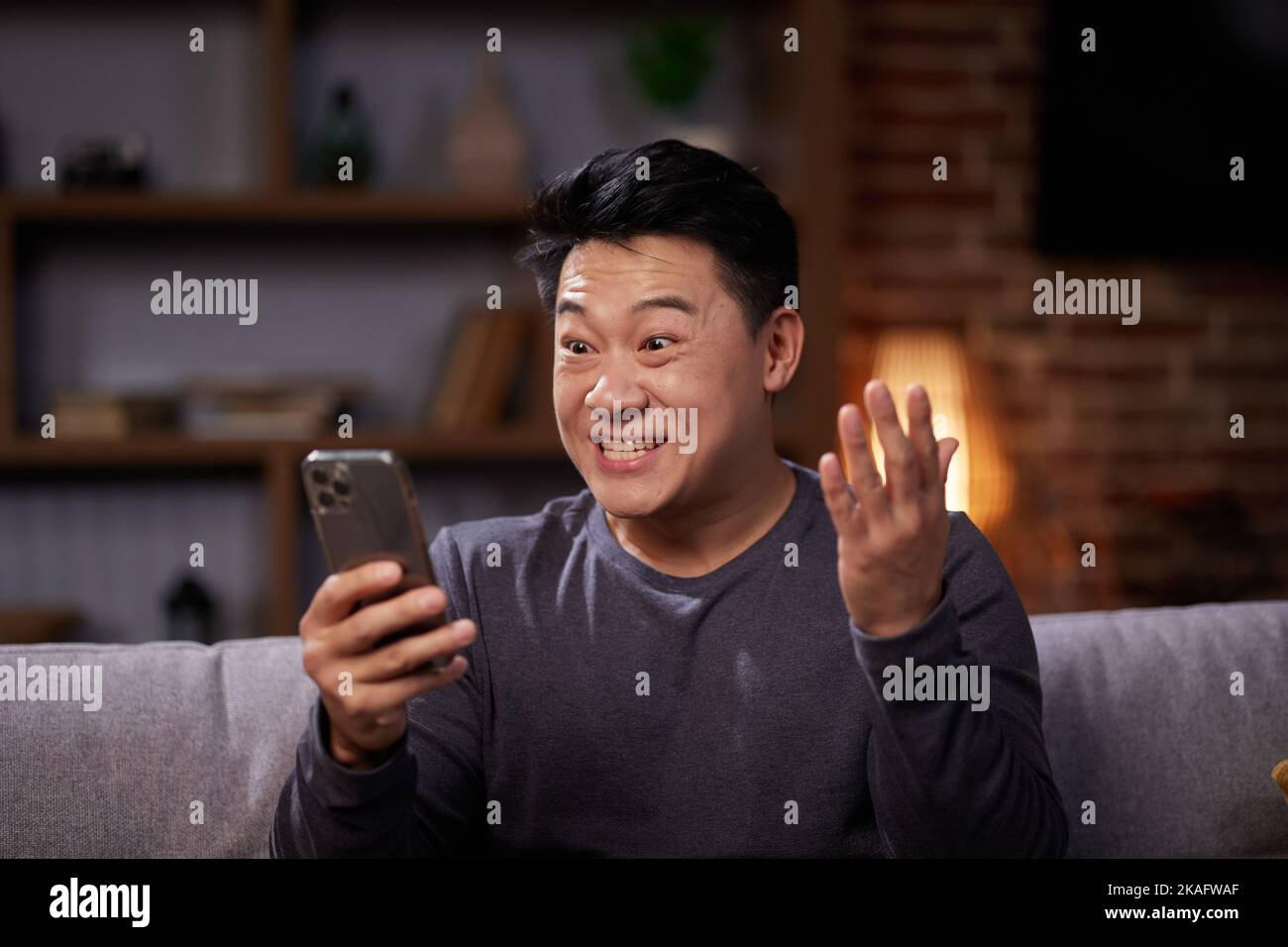 Asiatischer Mann feiert mobilen Erfolg mit Ja-Geste. Aufgeregt asiatischen Mann immer gute Nachrichten, machen Gewinner Geste und Blick auf den Telefonbildschirm Stockfoto